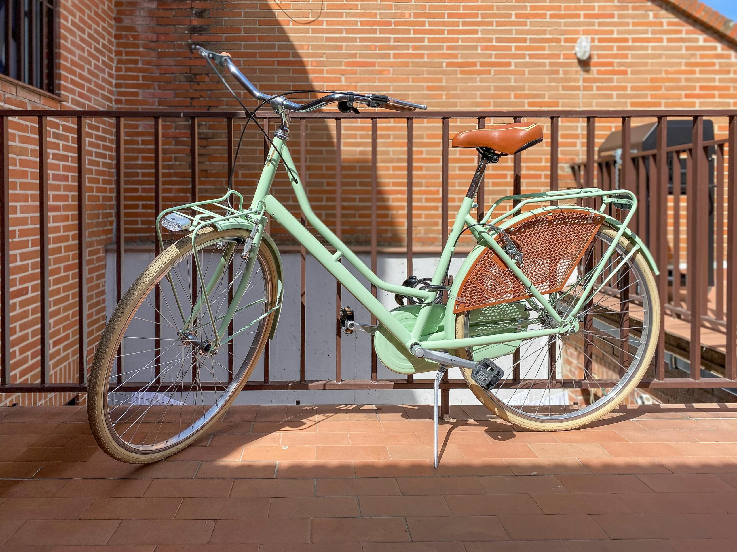 Classic green bicycle with leather saddle leaning against metal railing outdoors.